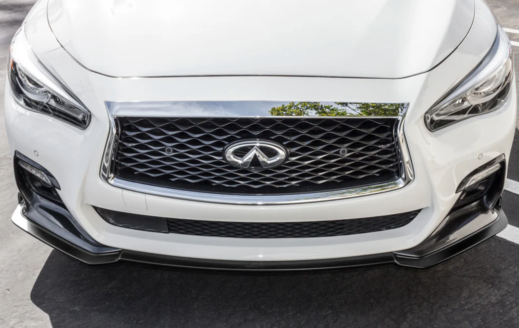 A front close up view of a white car fitted with Stillen Front Splitter [UNPAINTED] for Infiniti Q50 2018-2024 on the ground