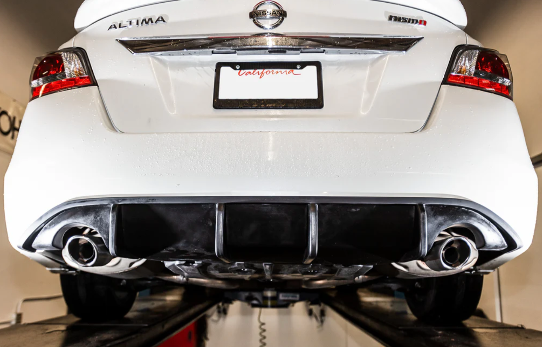 A back close up view of a white car fitted with Stillen Rear Diffuser [Matte Black] for Nissan Altima 2013-2015 on a lifted car