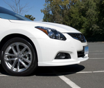 A side close up view of a white car fitted with Stillen Front Lip Spoiler for Nissan Altima Coupe 2010-2013 on the ground