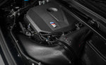A top side view of an open bonnet of a car fitted with Eventuri Black Carbon Intake System for BMW F7X M135i M235i / U1X X1 X2 M35i & MINI F6X S JCW 2020-2025 on the ground