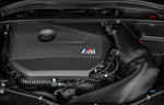 A close up view of an open bonnet of a car fitted with Eventuri Black Carbon Intake System for BMW F7X M135i M235i / U1X X1 X2 M35i & MINI F6X S JCW 2020-2025 on the ground