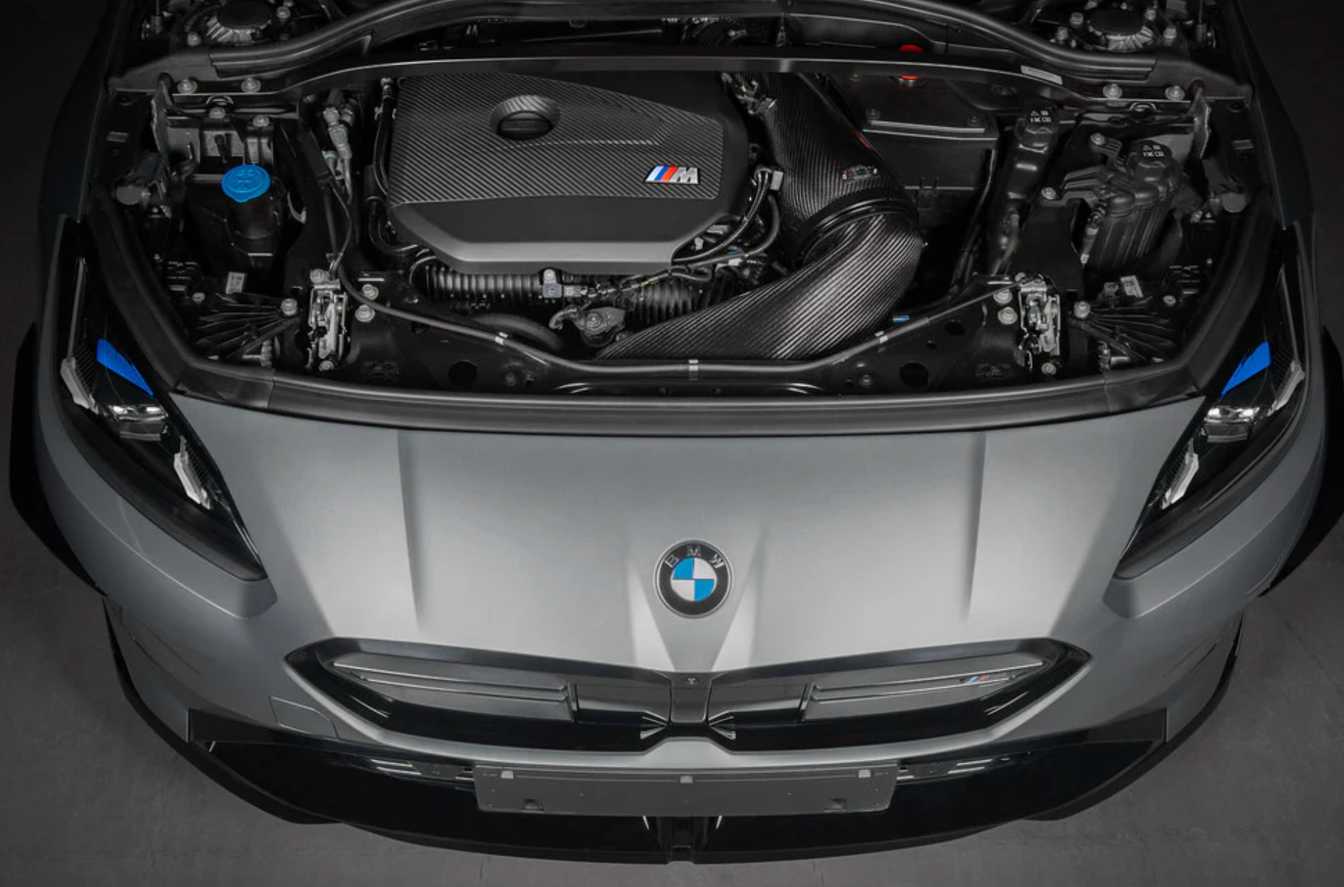 A top wide view of an open bonnet of a car fitted with Eventuri Black Carbon Intake System for BMW F7X M135i M235i / U1X X1 X2 M35i & MINI F6X S JCW 2020-2025 on the ground
