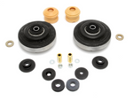 A collection of automotive suspension hardware arranged on a white background, including two large circular black rubber mounts with metal centers, two tan foam bump stops, several black rubber bushings of various sizes, two gold metal sleeves, and several silver metal washers and nuts.