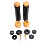 An automotive suspension kit featuring two long, black cylindrical tubes topped with tan foam bump stops. Below them are two additional standalone tan foam bump stops, six black rubber bushings of various sizes, two gold-toned metal sleeves, and four small silver hardware pieces including nuts and washers.