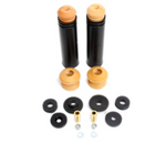 An automotive suspension kit featuring two long, black cylindrical tubes topped with tan foam bump stops. Below them are two additional standalone tan foam bump stops, six black rubber bushings of various sizes, two gold-toned metal sleeves, and four small silver hardware pieces including nuts and washers.