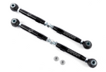 A pair of adjustable silver metal automotive suspension toe links laid horizontally on a white surface. Each link consists of a central hexagonal rod with a spherical rod end on one side and a mounting bracket on the other, accompanied by several silver metal spacers and two large black rubber dust boots.
