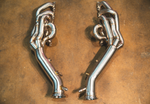 An overhead view of a symmetrical pair of polished stainless steel exhaust headers resting on a concrete floor.