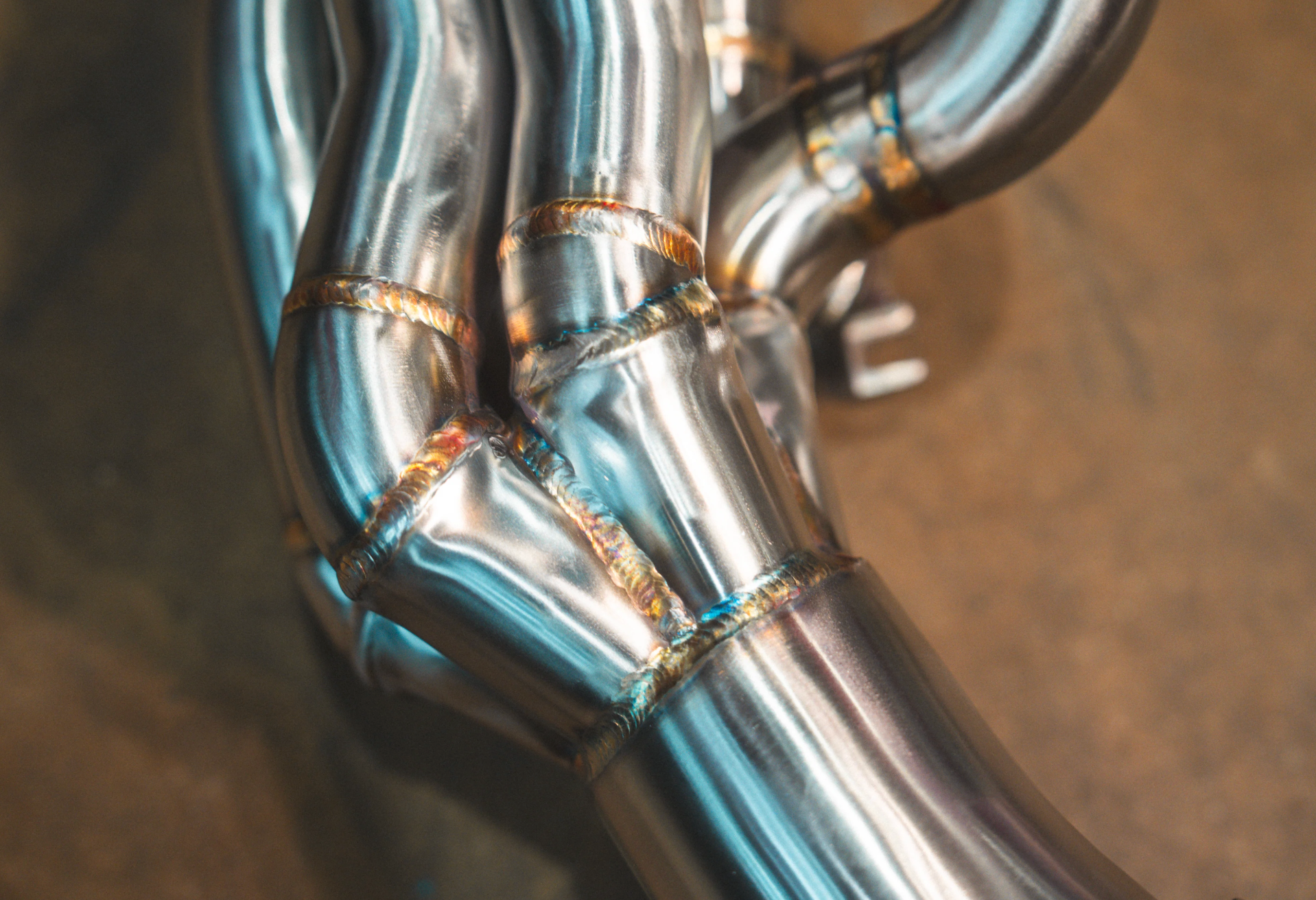 A close-up shot of polished stainless steel exhaust piping highlighting the detailed, heat-colored weld joints.
