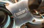 A close-up shot of a brushed metal identification plate welded to the exhaust system, featuring the "Valvetronic Designs Special Ops" logo and laser-etched product information.