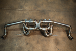 An angled overhead view of a polished stainless steel exhaust assembly highlighting the multi-pipe central crossover design and symmetrical piping.