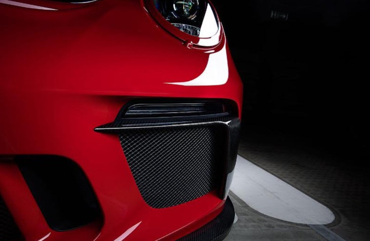 A close up view of TECHART Front Airblades Glossy Carbon Fiber Porsche 991.1 Turbo / S fitted on a red Porsche