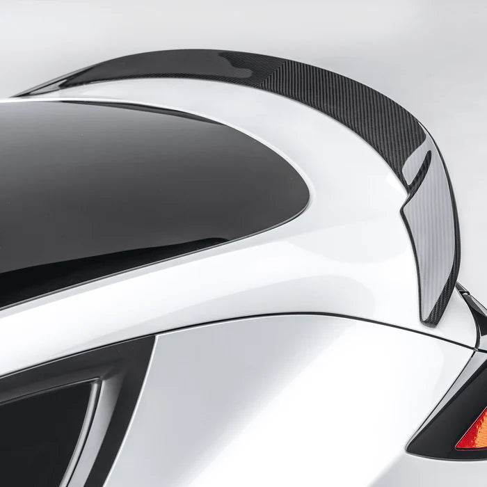 A close up view of Vorsteiner VRS Aero Decklid Spoiler Carbon Fiber PP 2x2 Glossy fitted on a white car (for Model Y).