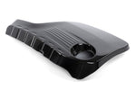 A high-gloss carbon fiber engine cover for BMW F8X models, featuring a classic 2x2 weave pattern. The cover shows a sculpted design with a circular cutout for the oil filler cap and integrated cooling fins on the top surface.