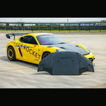Carbon fiber aeroshield panel laid out in front of a yellow track-prepped sports car showing the complete shape and surface area - SilverRocket Ultra Downforce Front Aeroshield Porsche 718 GT4 RS