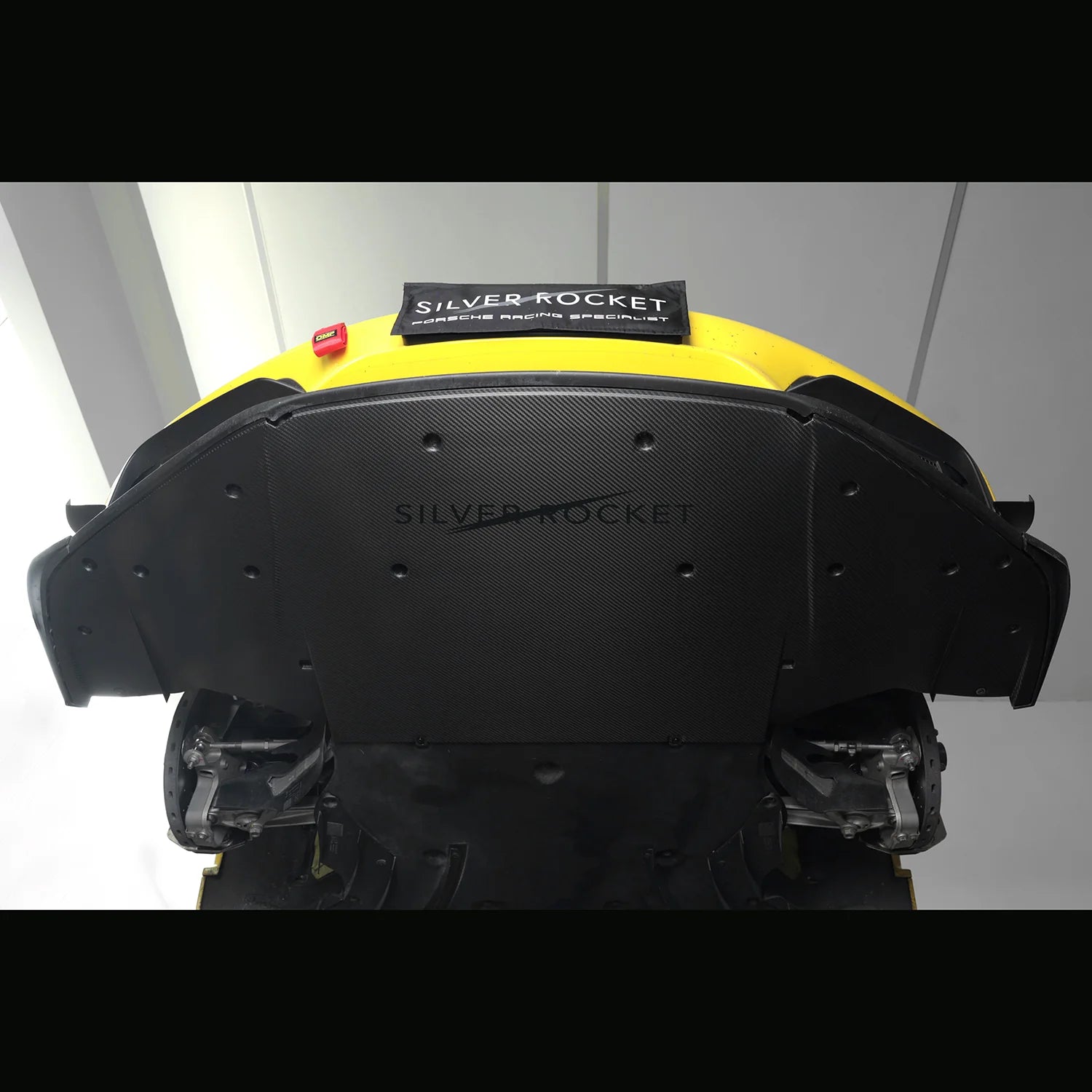 Underbody view of yellow sports car's front section with installed dry carbon fiber aeroshield panel showing visible twill weave covering the OEM aluminum tub - SilverRocket Ultra Downforce Front Aeroshield Porsche 718 GT4 RS