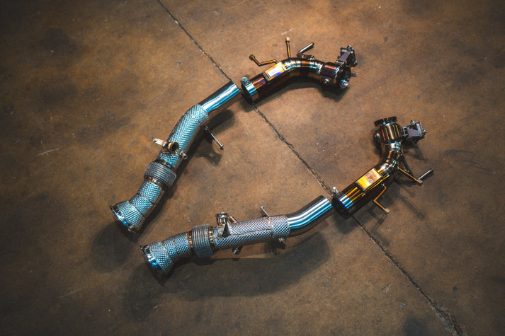 Ferrari 296 GTB GTS Valvetronic exhaust: pair of pipe sections with brackets on the shop floor, blue-tinted
