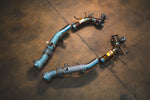 Ferrari 296 GTB GTS Valvetronic exhaust: pair of pipe sections with brackets on the shop floor, blue-tinted