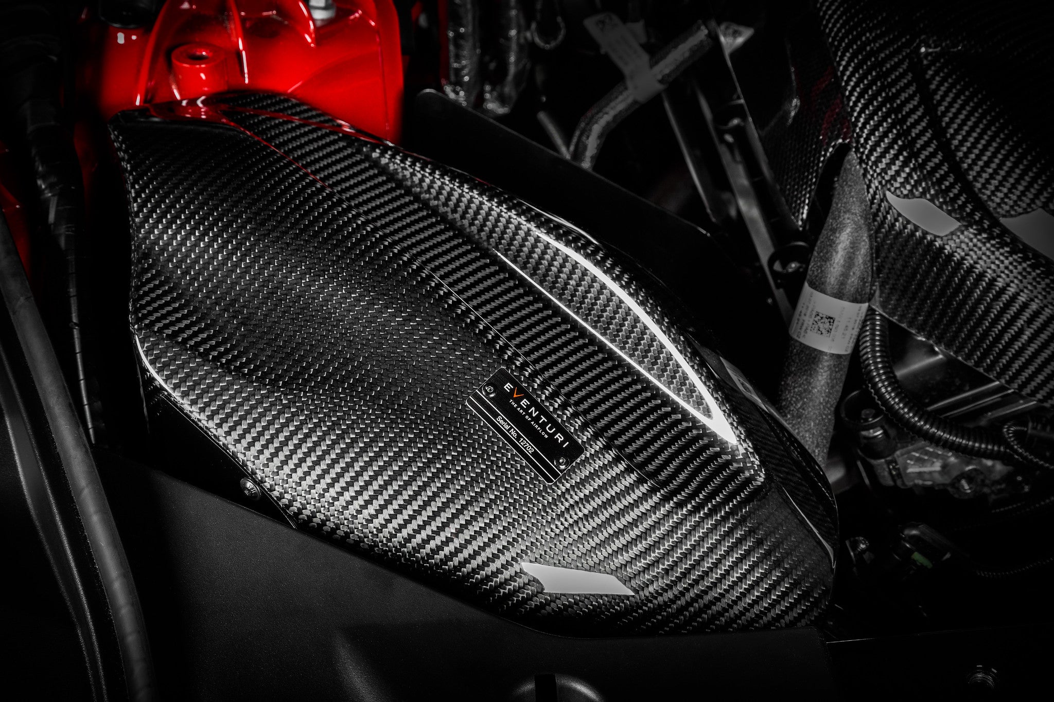 Carbon fiber intake system with weave pattern installed in engine bay with red engine cover visible - Eventuri intake for Toyota Supra