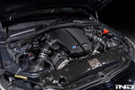 Black carbon fiber inlet plenum installed in BMW engine bay with carbon weave finish and blue M badge - Eventuri inlet plenum for BMW E60 M5 E63 M6