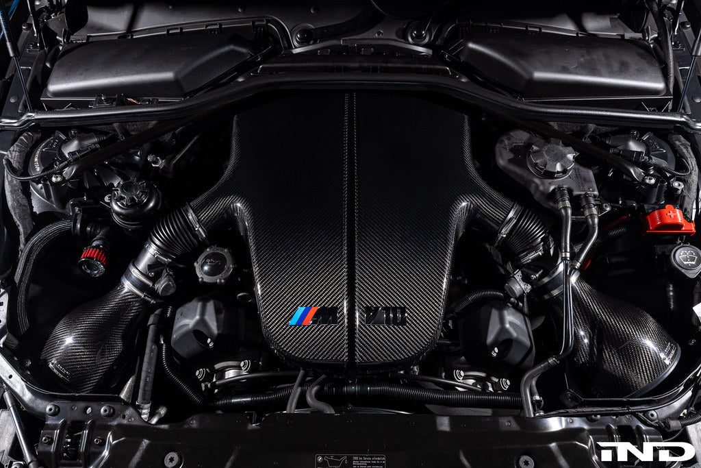 Large carbon fiber inlet plenum installed in engine bay with curved air ducts and BMW M badge - Eventuri inlet plenum for BMW E60 M5 E63 M6