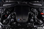 Large carbon fiber inlet plenum installed in engine bay with curved air ducts and BMW M badge - Eventuri inlet plenum for BMW E60 M5 E63 M6