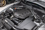 Black carbon fiber inlet plenum with curved design installed in BMW M3 engine bay with visible intake tubes - Eventuri inlet plenum for BMW M3