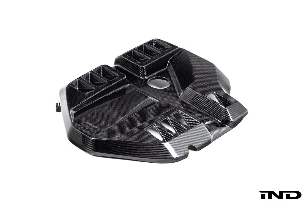 Black carbon fiber engine cover with geometric angular design and ventilation openings on white background - Eventuri engine cover for BMW M2