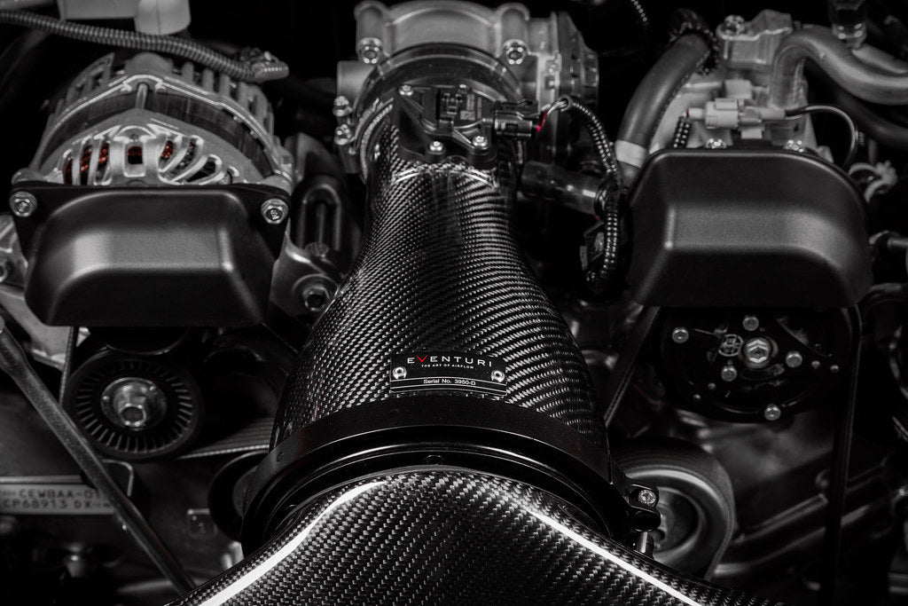 Carbon fiber intake tube with woven pattern installed in engine bay surrounded by metal components and hoses - Eventuri cold air intake for Toyota GR 86