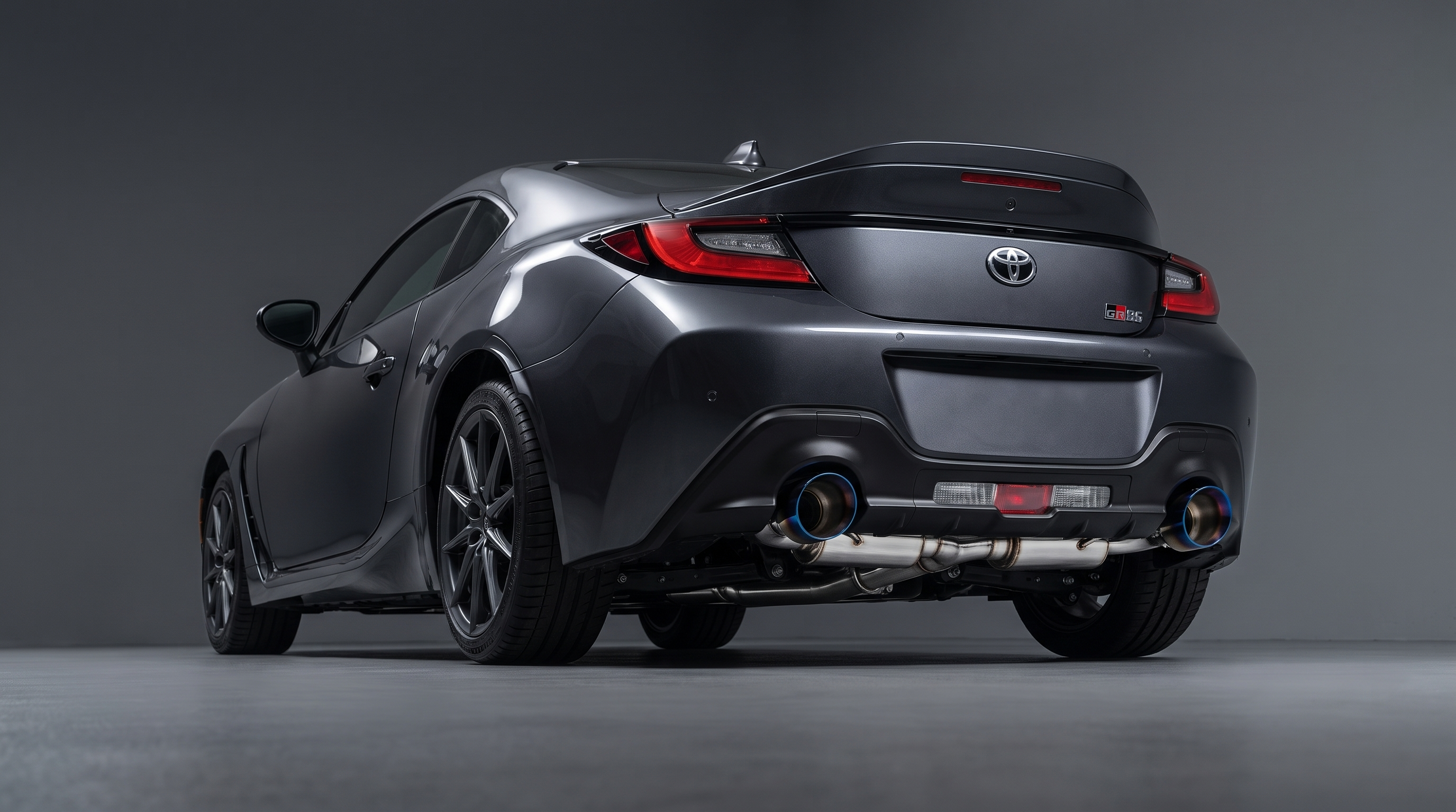 Toyota GR86 rear three-quarter studio photograph with an AWE-style cat-back exhaust installed, showing dual large slash-cut tips with blue-tinted rims