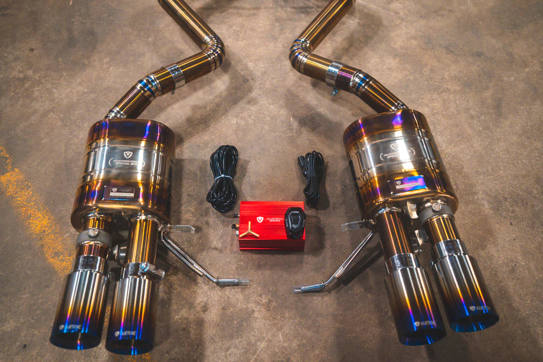 A close up view of Valvetronic Designs Titanium Valved Sport Exhaust System's mufflers, exhaust tips and valve controller, on the ground (for BMW M3 E9X).