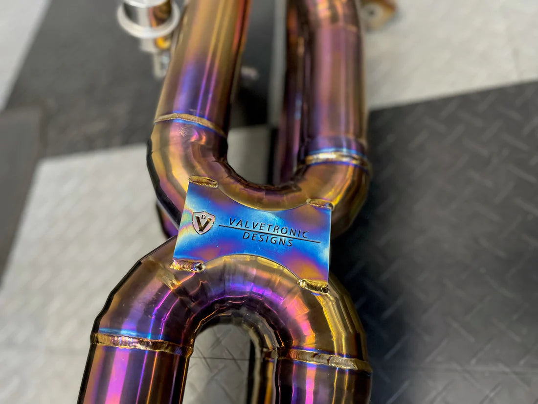 A close up of a part of Valvetronic Designs Valved Sport Exhaust System (for Audi R8 V10 / Lamborghini HuracanF1) showing the brand's logo on the ground.