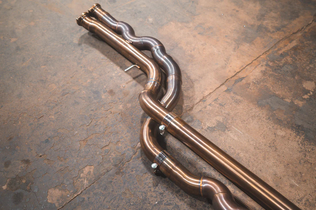 A wide view of Valvetronic Designs Equal Length Valved Sport Exhaust System's pipes on the ground (for BMW M3 F80, M4 F82, M4 F83).