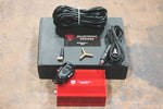 A top overview of Valvetronic Designs UNIVERSAL Valved Muffler Kit in a black and red box on the ground with wires.