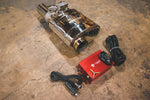 A titled top view of Valvetronic Designs UNIVERSAL Valved Muffler Kit on the ground with wires and red box.