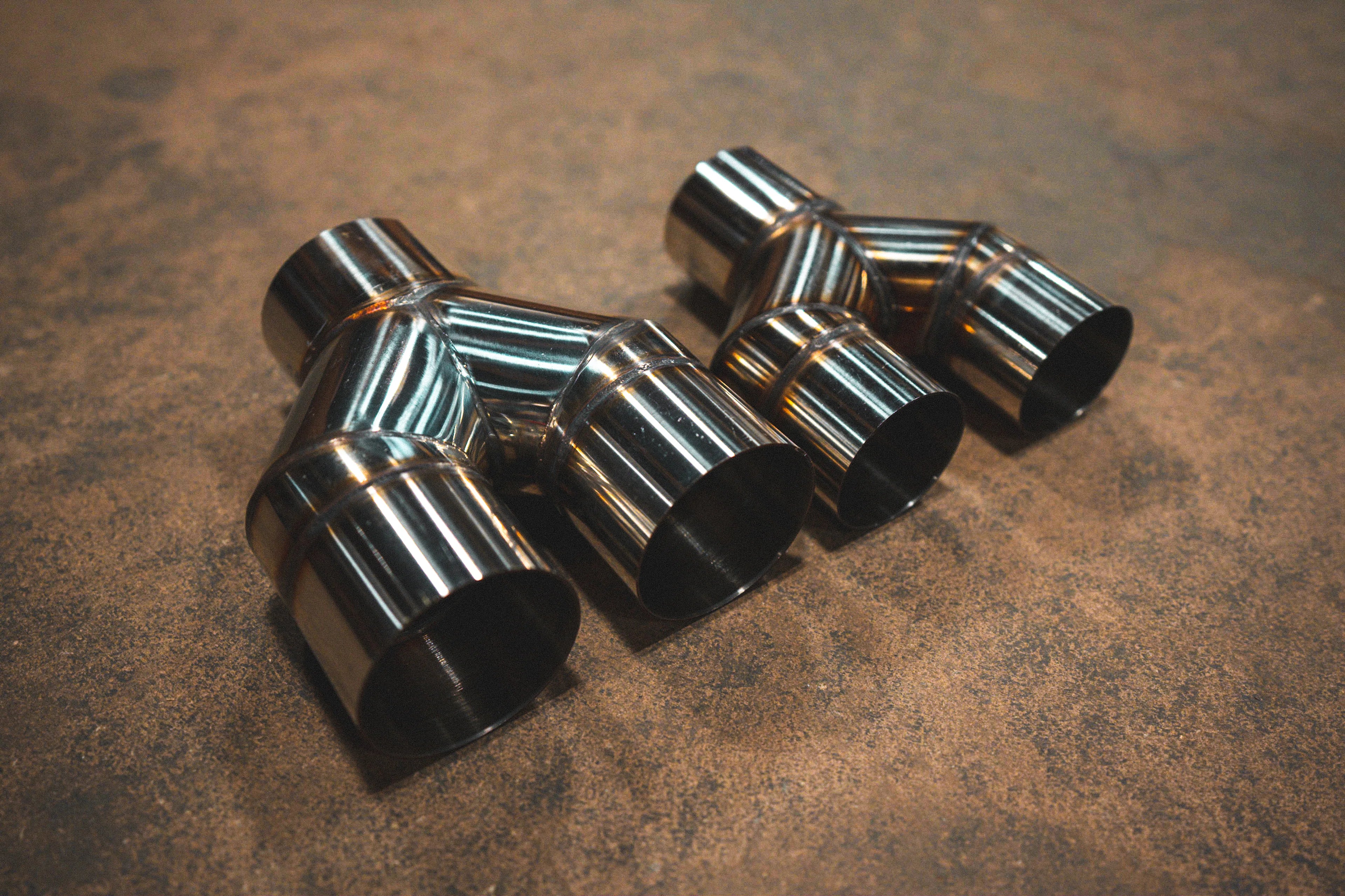 An angled close-up view of two stainless steel Y-pipe adapters with visible weld beads resting on a concrete floor.