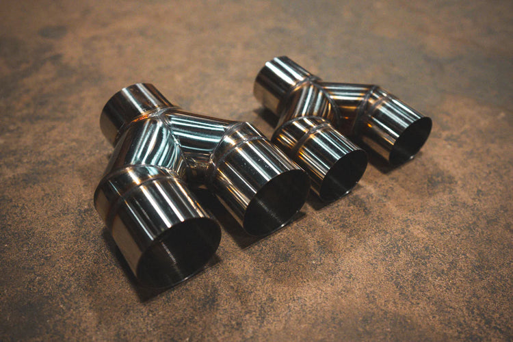 A side overview of Valvetronic Designs Universal Y Pipe Adapter in two sizes on the ground.