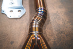 A close up view of Valvetronic Designs Equal Length Midpipe in Grade 5 Titanium on the ground (for BMW G8x M3 / M4).