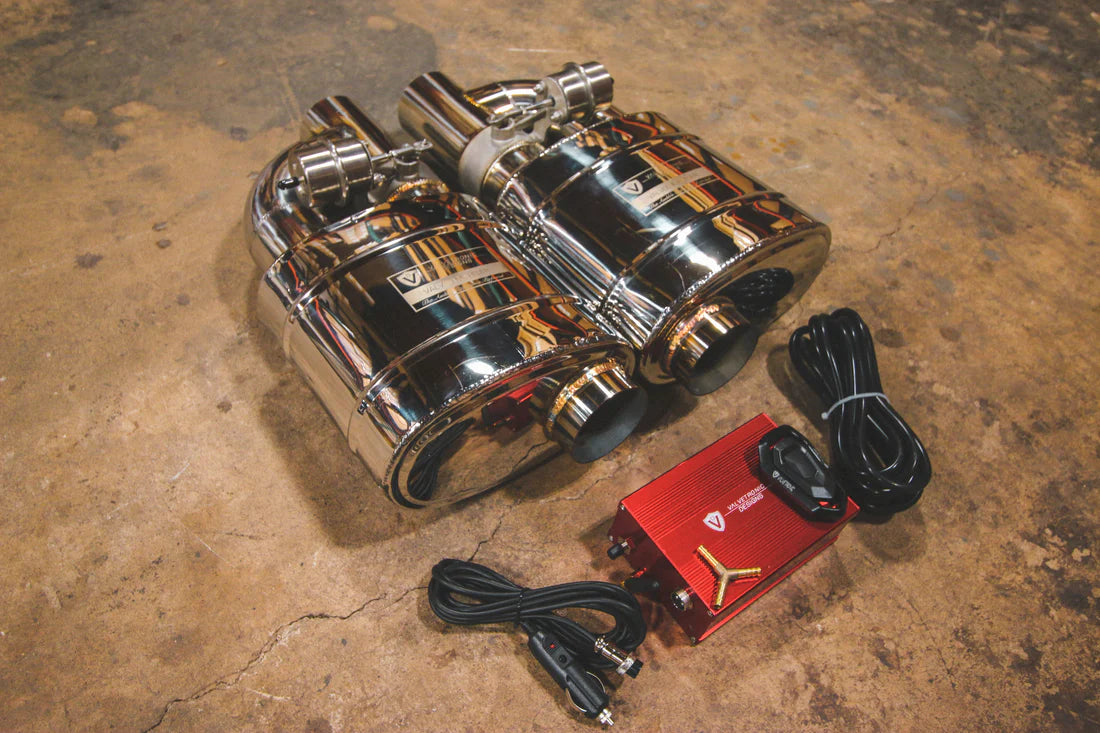 A top view of Valvetronic Designs UNIVERSAL Valved Muffler Kit with two mufflers on the ground with wires and red box.