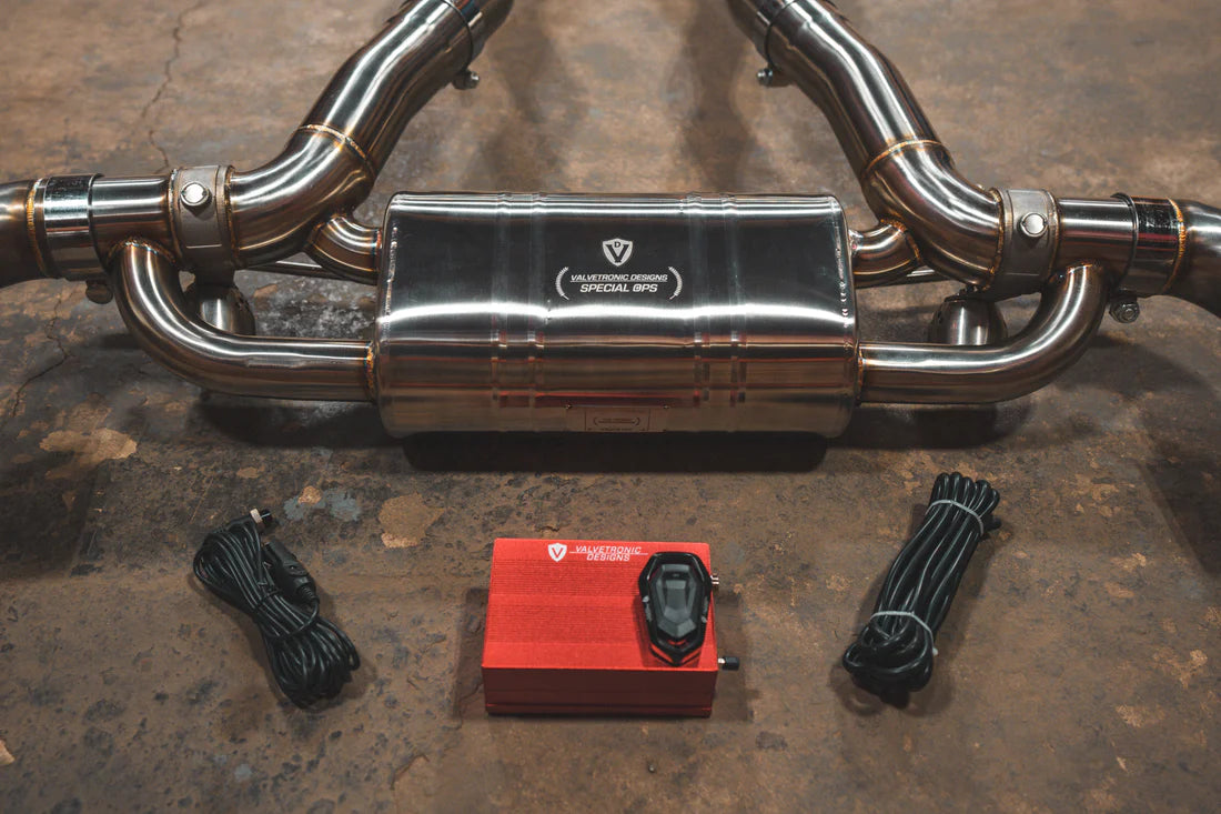 A close up view of Valvetronic Designs Brushed Valved Sport Exhaust System with valve controllers and wires on the ground (for Toyota Supra A90 / A91).