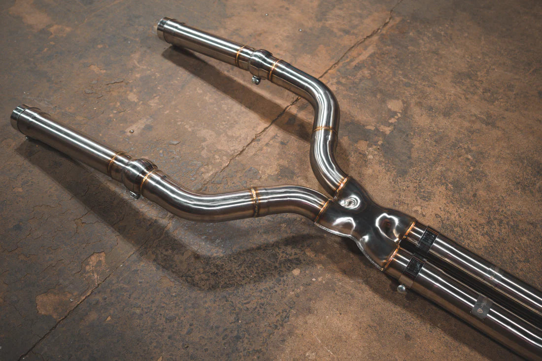 A close view of Valvetronic Designs Valved Sport Exhaust System's pipes on the ground (for BMW F90 M5). 