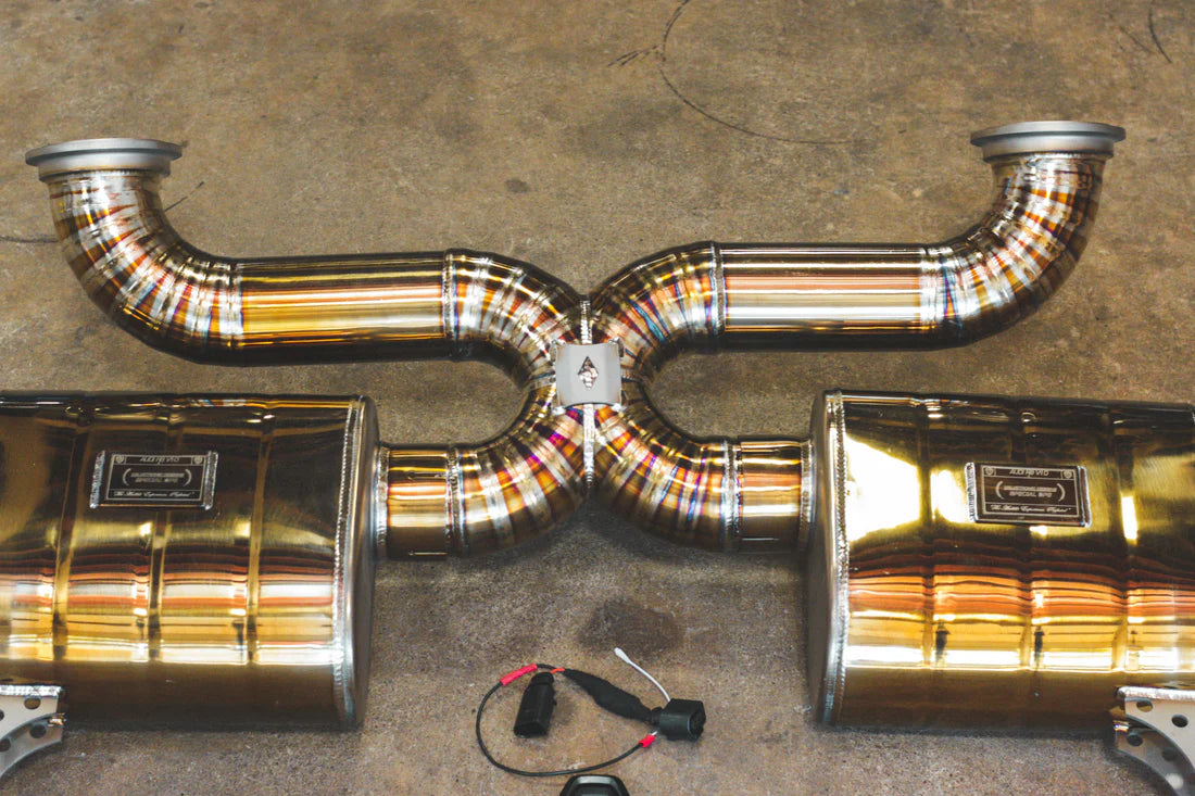 A horizontal view of Valvetronic Designs gold Valved Sport Exhaust System (for Audi R8 V10 Gen 2 2017+)  with wires on the ground.