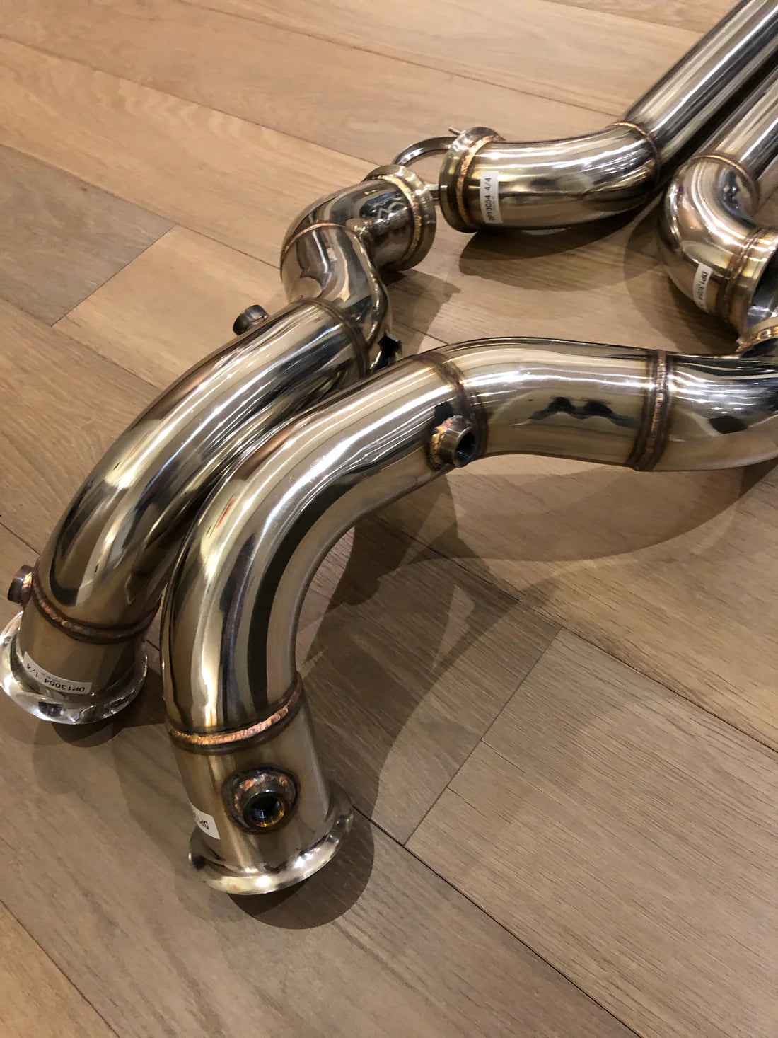 A close up view of Valvetronic Designs Free Flow Front Pipes on a wooden floor (for Mercedes AMG GT/ GTC / GTR).