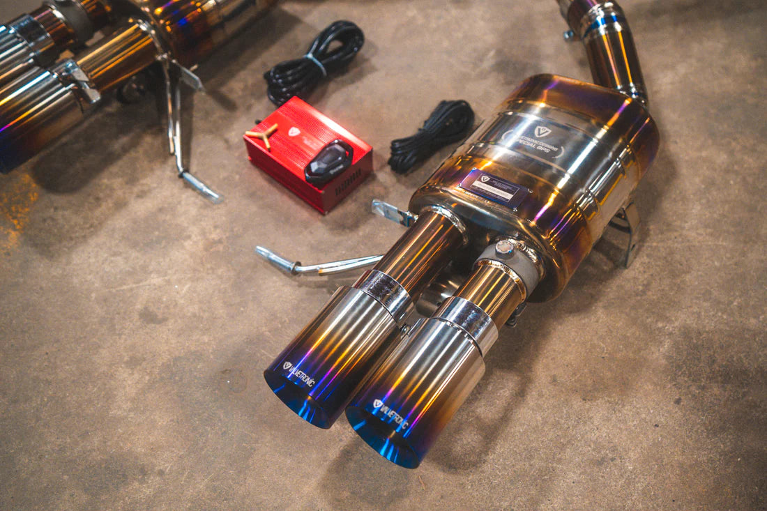 A close up view from the top of Valvetronic Designs Titanium Valved Sport Exhaust System's one muffler, exhaust tips and valve controller, on the ground (for BMW M3 E9X).