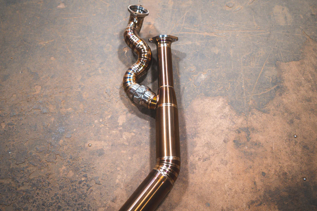 A close up view of Valvetronic Designs Equal Length Midpipe in Grade 5 Titanium on the ground (for BMW G8x M3 / M4).