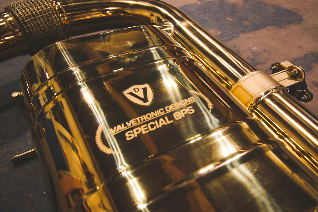 A close up view of Valvetronic Designs Valved Sport Exhaust System's muffler, showing the brand's logo, on the ground (for BMW i8). 