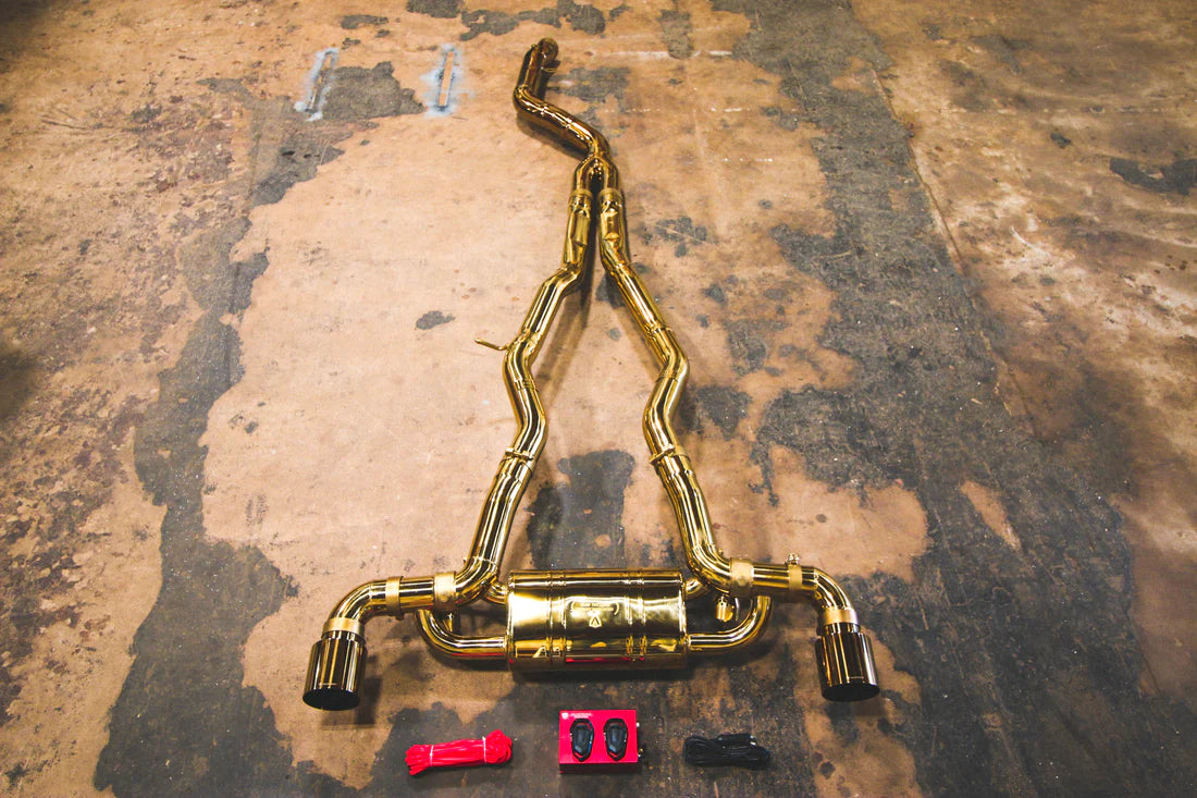 A wide view of Valvetronic Designs Anodized Gold Valved Sport Exhaust System with valve controller and wires on the ground (for Toyota Supra A90 / A91).