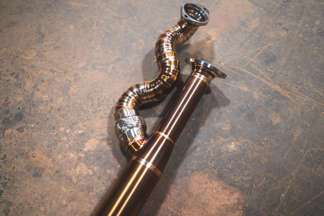 A close up view of Valvetronic Designs Equal Length Midpipe in Grade 5 Titanium on the ground (for BMW G8x M3 / M4).