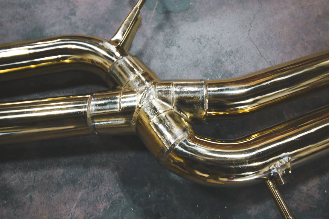 A close up of Valvetronic Designs gold Valved Sport Exhaust Sytem pipes (for Audi RS6 / RS7 C7) on the ground.