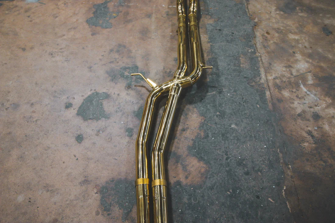 A close up of pipes of Valvetronic Designs gold Valved Sport Exhaust Sytem (for Audi RS6 / RS7 C7) on the ground.