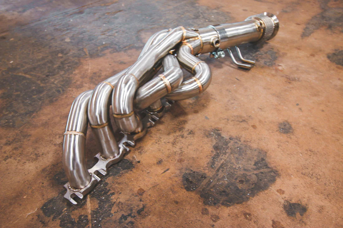 An overview of one Valvetronic Designs Free Flow Headers (for Audi R8 V10 / Lamborghini Gallardo LP / Lamborghini Huracan) exhaust pipe on the ground.  